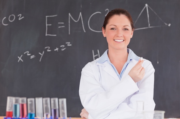 Young scientist holding a piece of chalk while standing in front of a blackboard