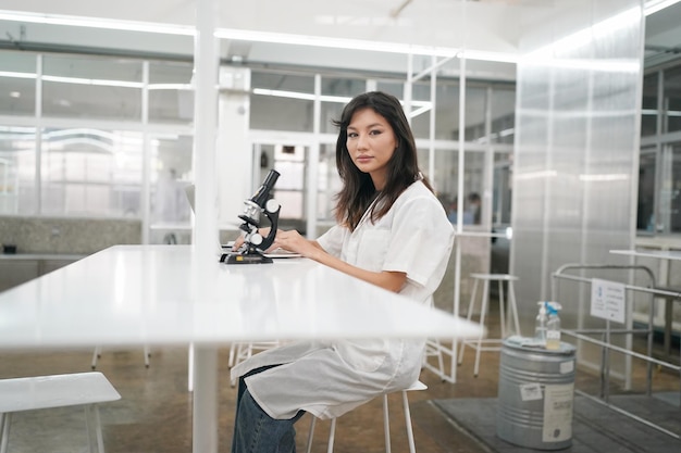 Young scientist in white lab coat working with binocular\
microscope in the material science lab