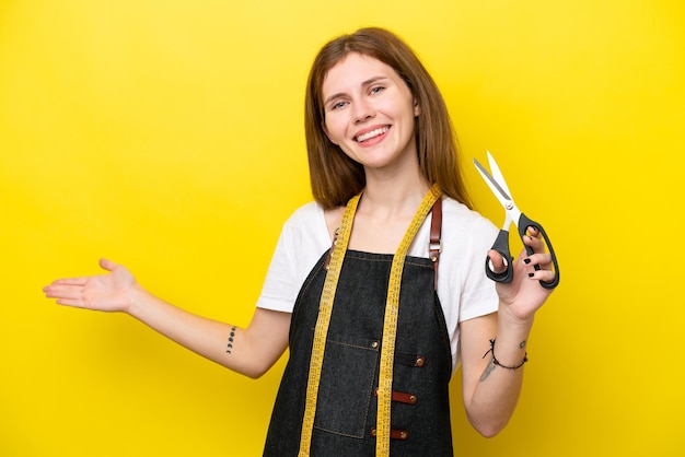 Giovane sarta donna inglese isolata su sfondo giallo che estende le mani di lato per invitare a venire