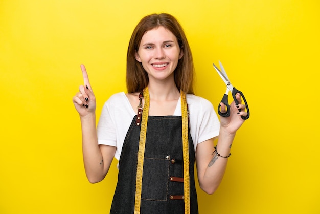 Young seamstress English woman isolated on yellow background showing and lifting a finger in sign of the best