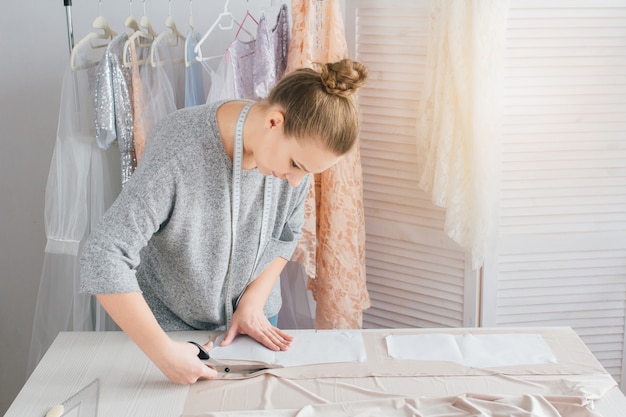 若い女性の裁縫師は服を切る服を作る