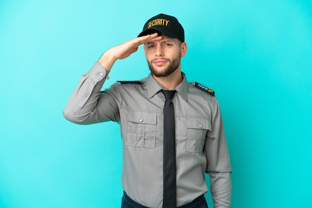 Young security man isolated on blue background looking far away with hand to look something