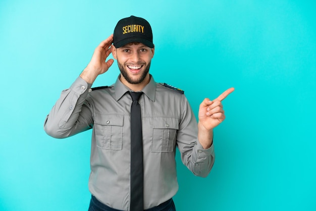 Young security man isolated on blue background surprised and pointing finger to the side
