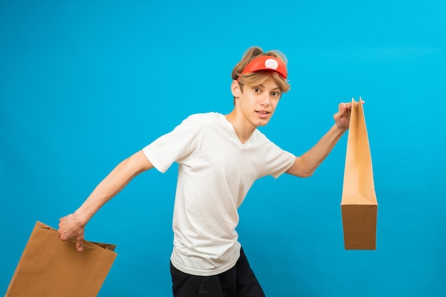 Young seller in casual white tshirt with paper bag running on blue background studio portrait People lifestyle concept Mock up copy space Teen holding package bag with purchases