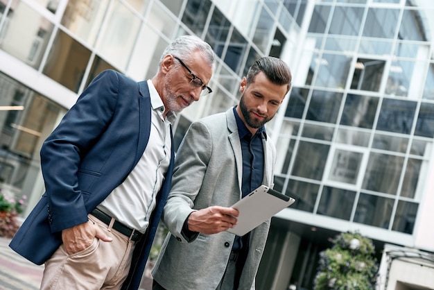 Young and senior business men using digital tablet outdoors on the city background