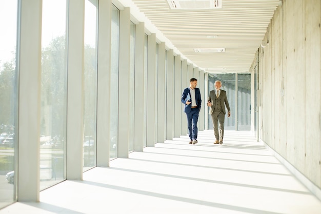 Young and a senior businessman walk down an office hallway deep in conversation