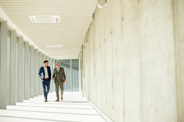 Young and a senior businessman walk down an office hallway deep in conversation