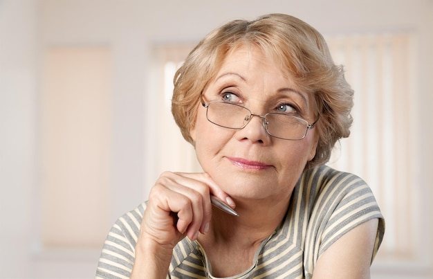 Young senior woman holding pen and thinking