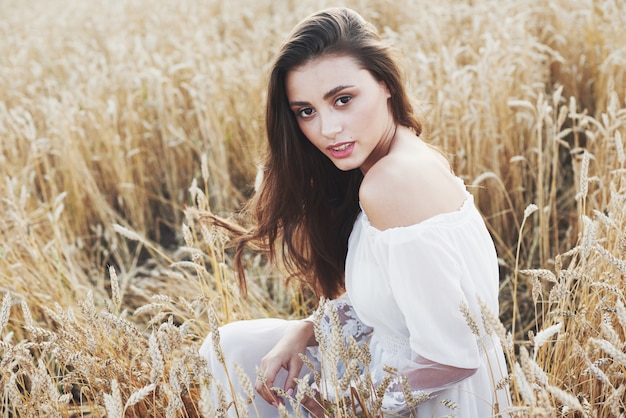 Young sensitive woman in white dress posing in a field of golden wheat