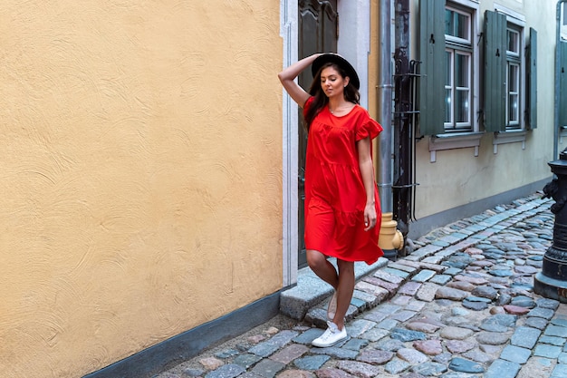 A young sensual woman in a red dress and a black hat on a\
cobbled old town street