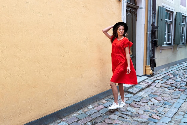 A young sensual woman in a red dress and a black hat on a cobbled old town street