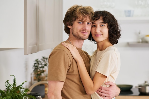 Young serene couple standing in embrace in the kitchen