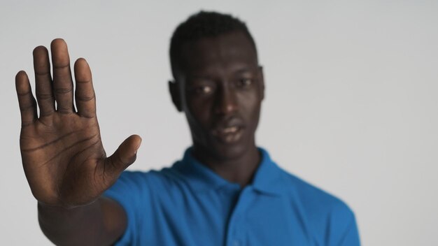 Young serious African American man showing hand in camera over white background Conceptual shot