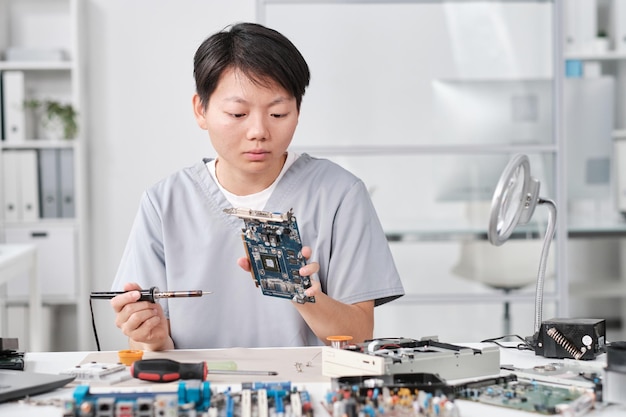Young serious asian woman with soldering iron looking at hardware