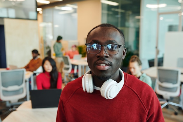 Young serious businessman or designer of African ethnicity holding smartphone by ear while talking to client in working environment