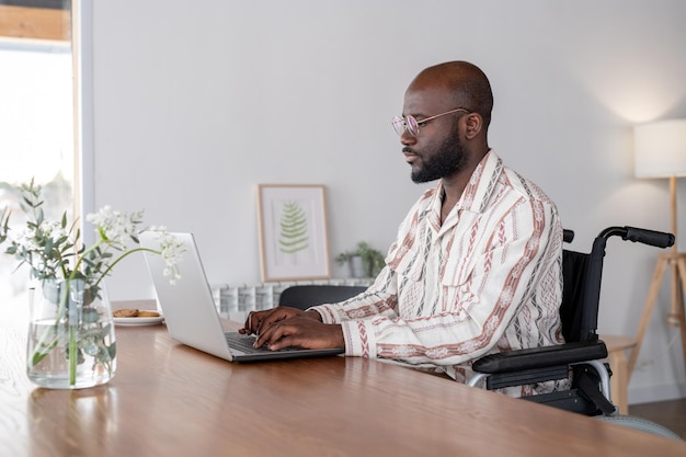 Young serious businessman in wheelchair looking at laptop screen while typing