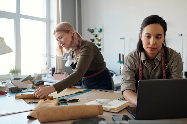 Young serious businesswoman sitting by workplace in front of laptop