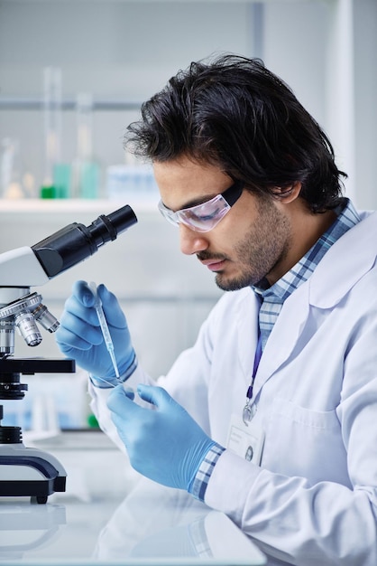 Young serious chemist in labcoat dropping liquid substance into petri dish