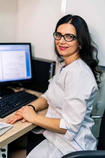 Young serious competent female doctor looking at camera at doctor's office Medical office background