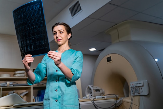 Photo young serious competent female doctor looking at x-ray at doctor's office. computer tomography background.