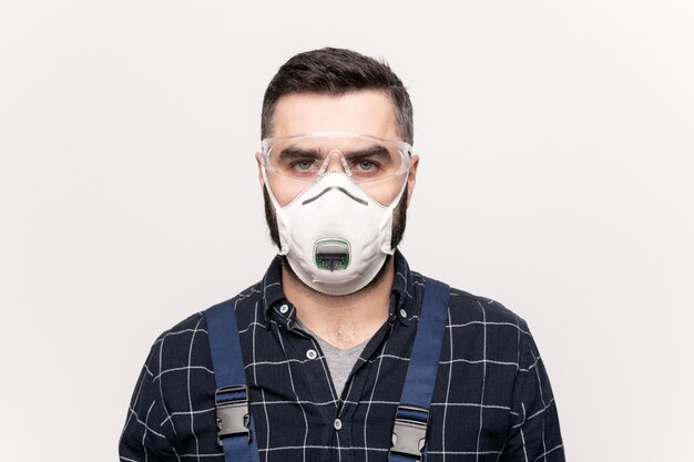 Young serious engineer or repairman in workwear, protective eyeglasses and respirator