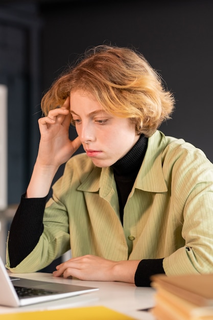 Фото Молодая серьезная женщина-разработчик программного обеспечения сидит за столом и просматривает онлайн-информацию на дисплее ноутбука во время работы в сети
