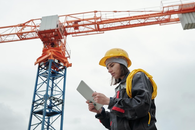 Young serious female engineer in workwear looking at screen of\
tablet