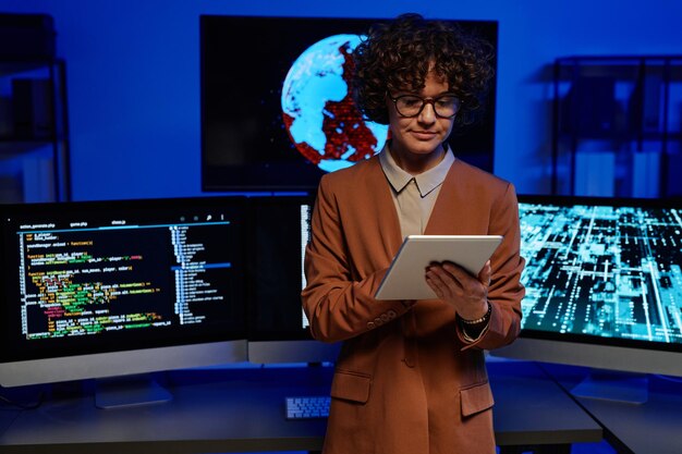 Young serious female programmer using tablet against computers