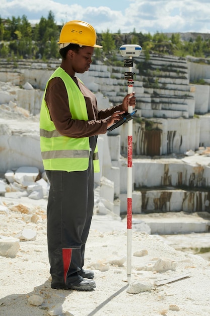 Young serious female surveyor in workwear choosing settings of theodolite