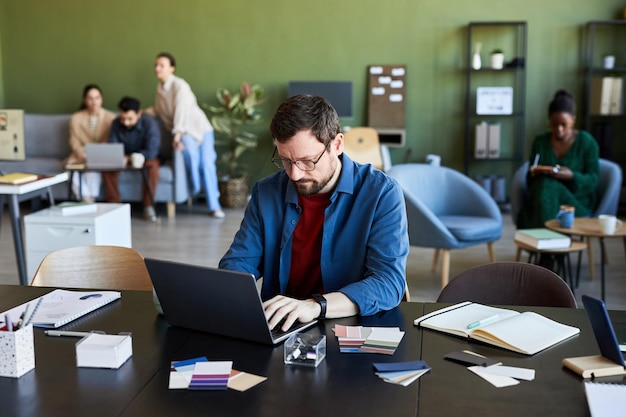 Young serious male designer looking at laptop screen while\
watching online video or training about s