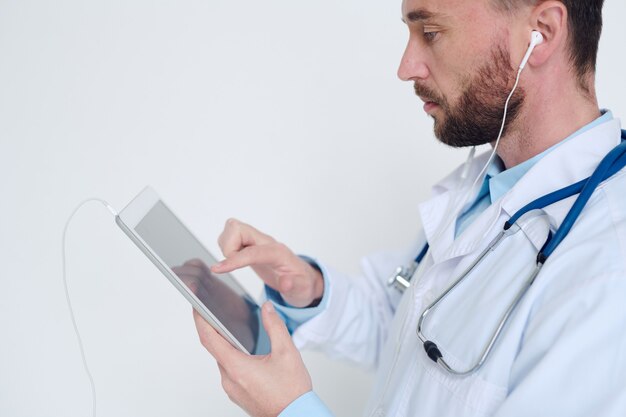 Young serious male doctor in earphones pointing at digital tablet while taking online patients and giving them medical recommendations