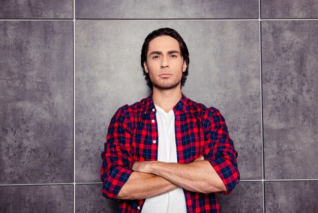 Young serious man with crossed hands isolated on gray space