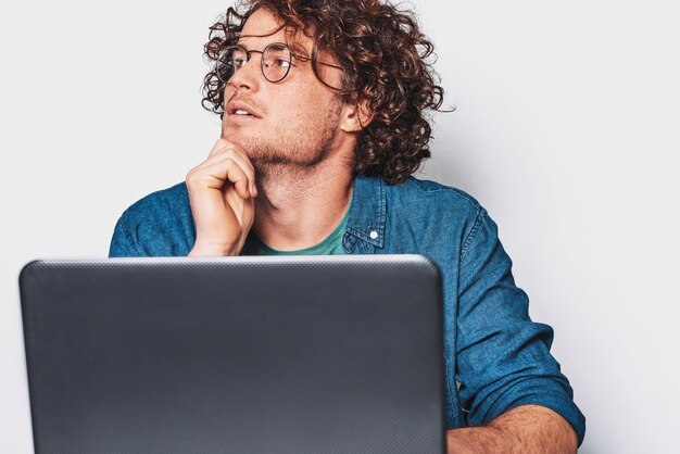 곱슬 머리를 가진 젊은 진지한 남자 노트북에서 작업 하 고 생각 사업가 라운드 안경을 쓰고 노트북 컴퓨터에서 작업 테이블에 앉아