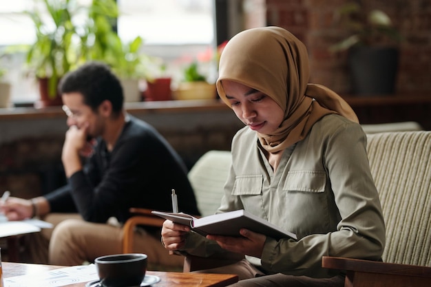 Young serious muslim businesswoman in hijab looking through notes