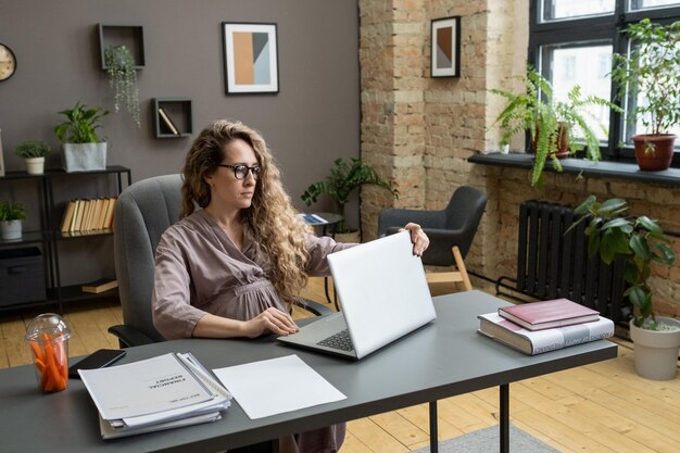 Young serious pregnant businesswoman opening laptop before working