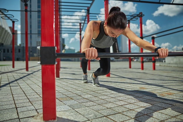 Young serious sportswoman bowing head while counting amount of pushups from the bar