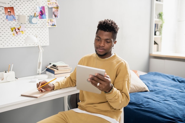 Young serious student in casualwear looking at tablet screen