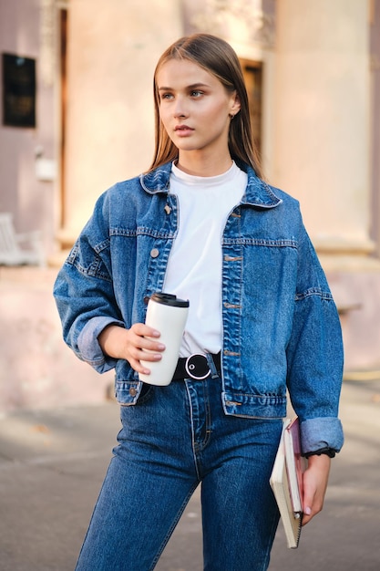 Giovane studentessa seria ed elegante in giacca di jeans distoglie lo sguardo pensieroso all'aperto