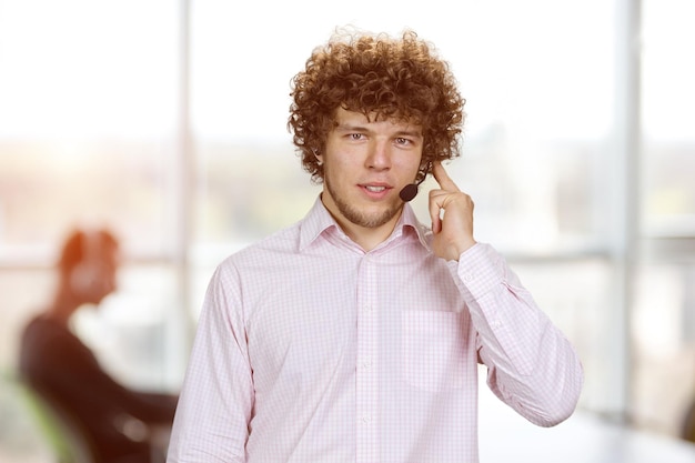 Фото Молодой серьезный успешный мужчина с кудрявыми волосами говорит в микрофоне интерьера офиса на заднем плане