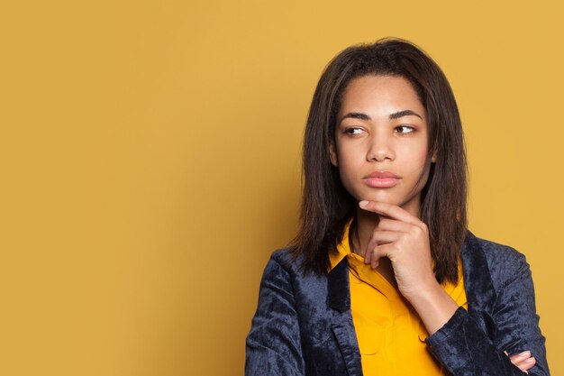 Young serious woman thinking on yellow background