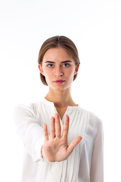 Young serious woman in white blouse holding hand in front of her on white background in studio