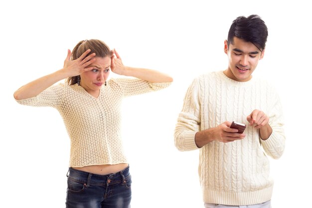 Young serious woman with long chestnut ponytail arguing with young smiling man in white sweater