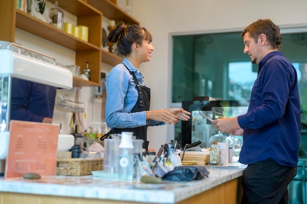 コーヒーショップで顧客と若いサービス志向のバリスタ女性