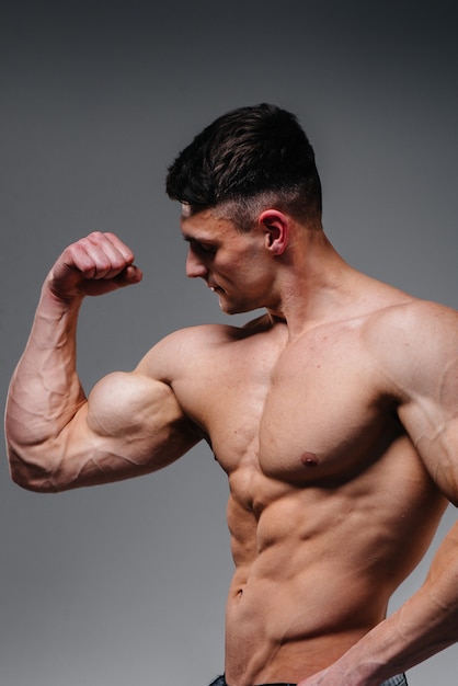 A young sexy athlete with perfect abs poses in the studio topless in jeans on the background. Healthy lifestyle, proper nutrition, training programs and nutrition for weight loss.