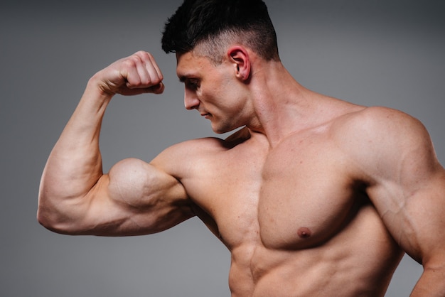 A young sexy athlete with perfect abs poses in the studio topless in jeans on the background. Healthy lifestyle, proper nutrition, training programs and nutrition for weight loss.