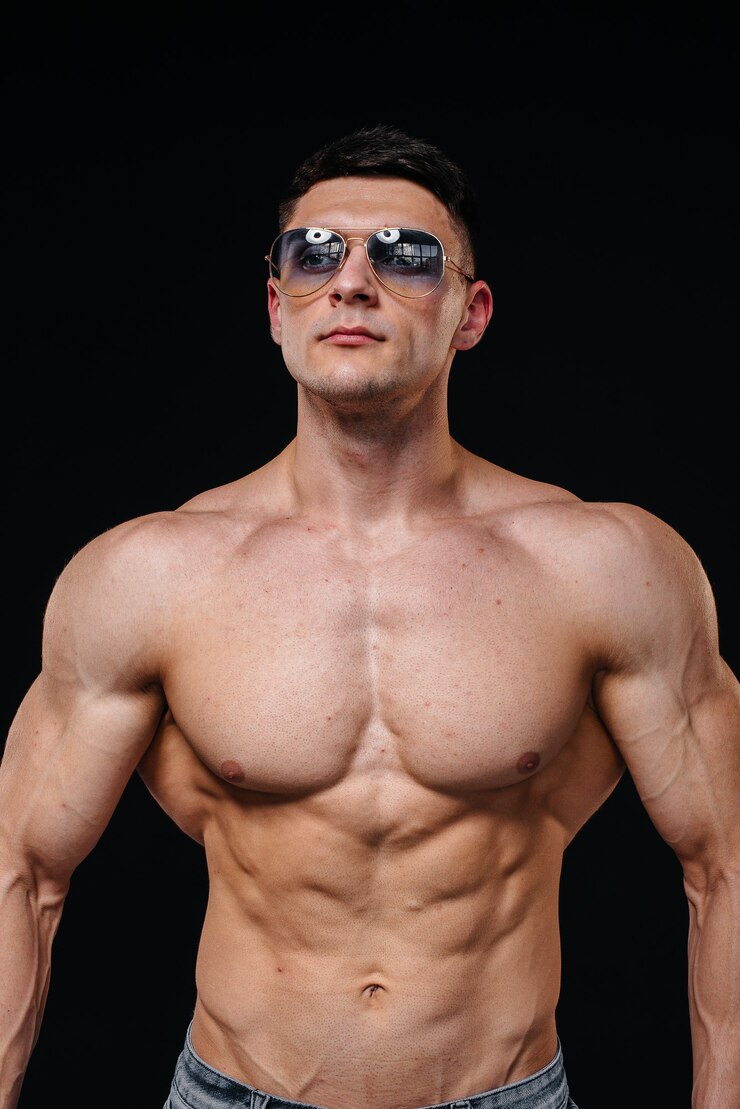 A young sexy athlete with perfect abs poses in the studio topless in jeans in a pair of protective glasses. Healthy lifestyle, proper nutrition, training programs and nutrition for weight loss.