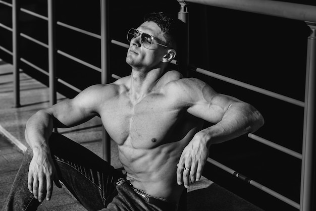 A young sexy athlete with perfect abs poses topless in jeans outside on a sunny day. Healthy lifestyle, proper nutrition, training programs and nutrition for weight loss. Black and white.