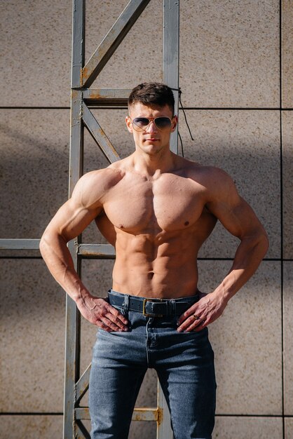 A young sexy athlete with perfect abs poses topless in jeans outside on a sunny day. Healthy lifestyle, proper nutrition, training programs and nutrition for weight loss.