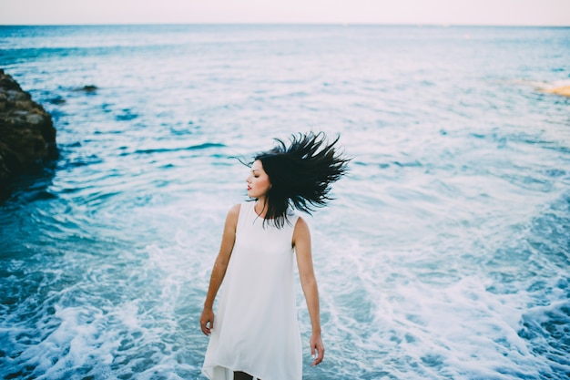 그리스의 해변에 하얀 드레스를 입고 푸른 물에 젊은 섹시한 갈색 머리