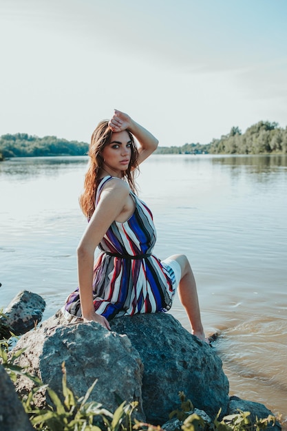 Young sexy girl in a light summer dress looking back over her shoulder sitting by the river